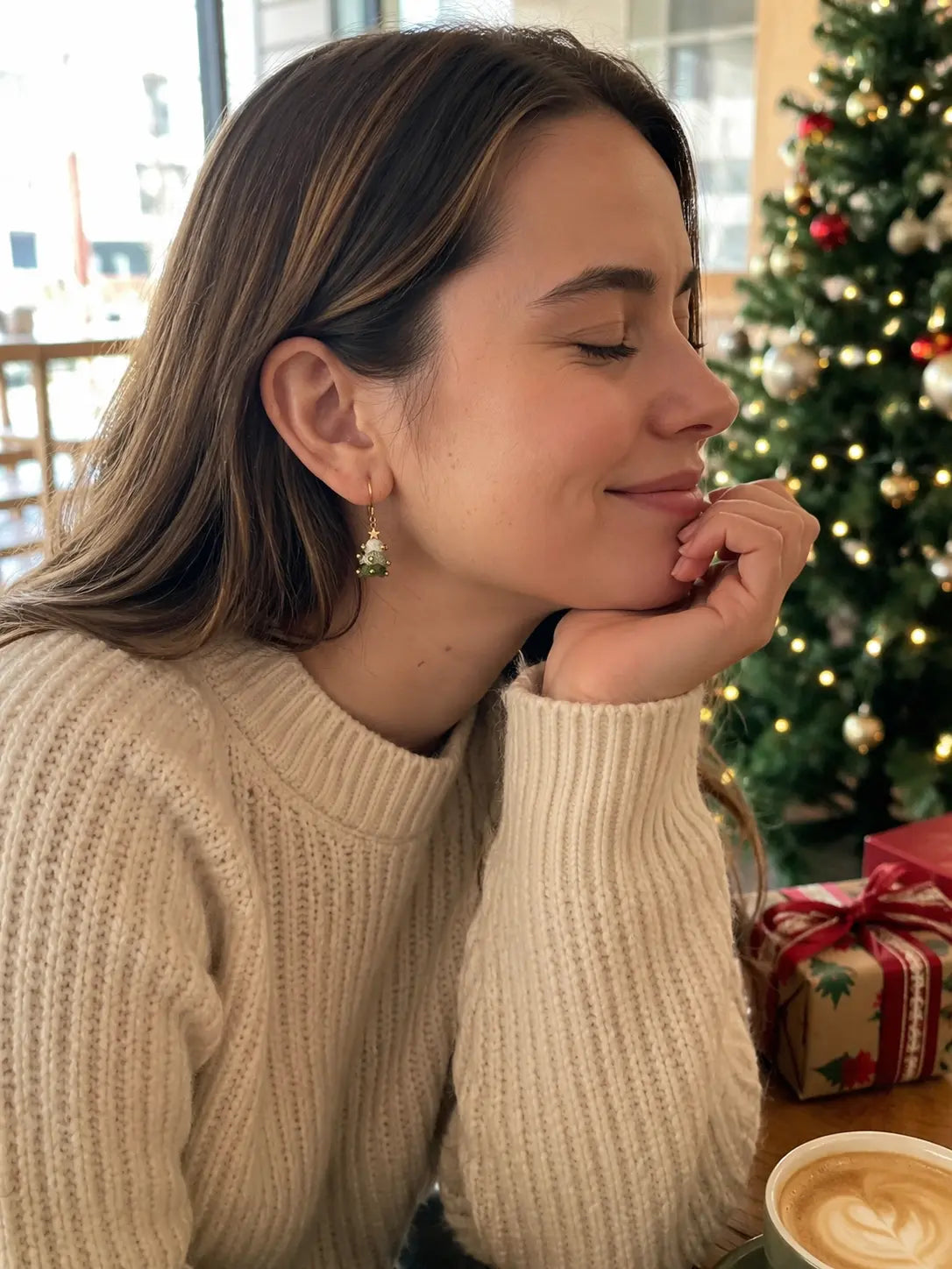 Woman wearing handmade Christmas tree crochet earrings in a cosy cafe with festive Christmas decor
