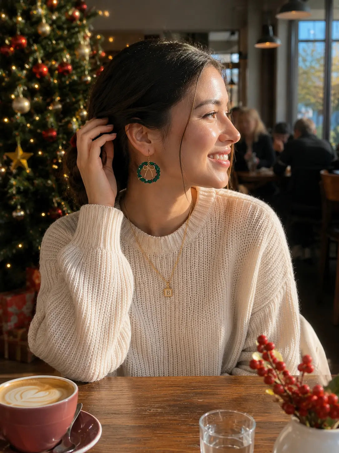 Woman wearing green Christmas wreath crochet earrings in a warm holiday cafe setting