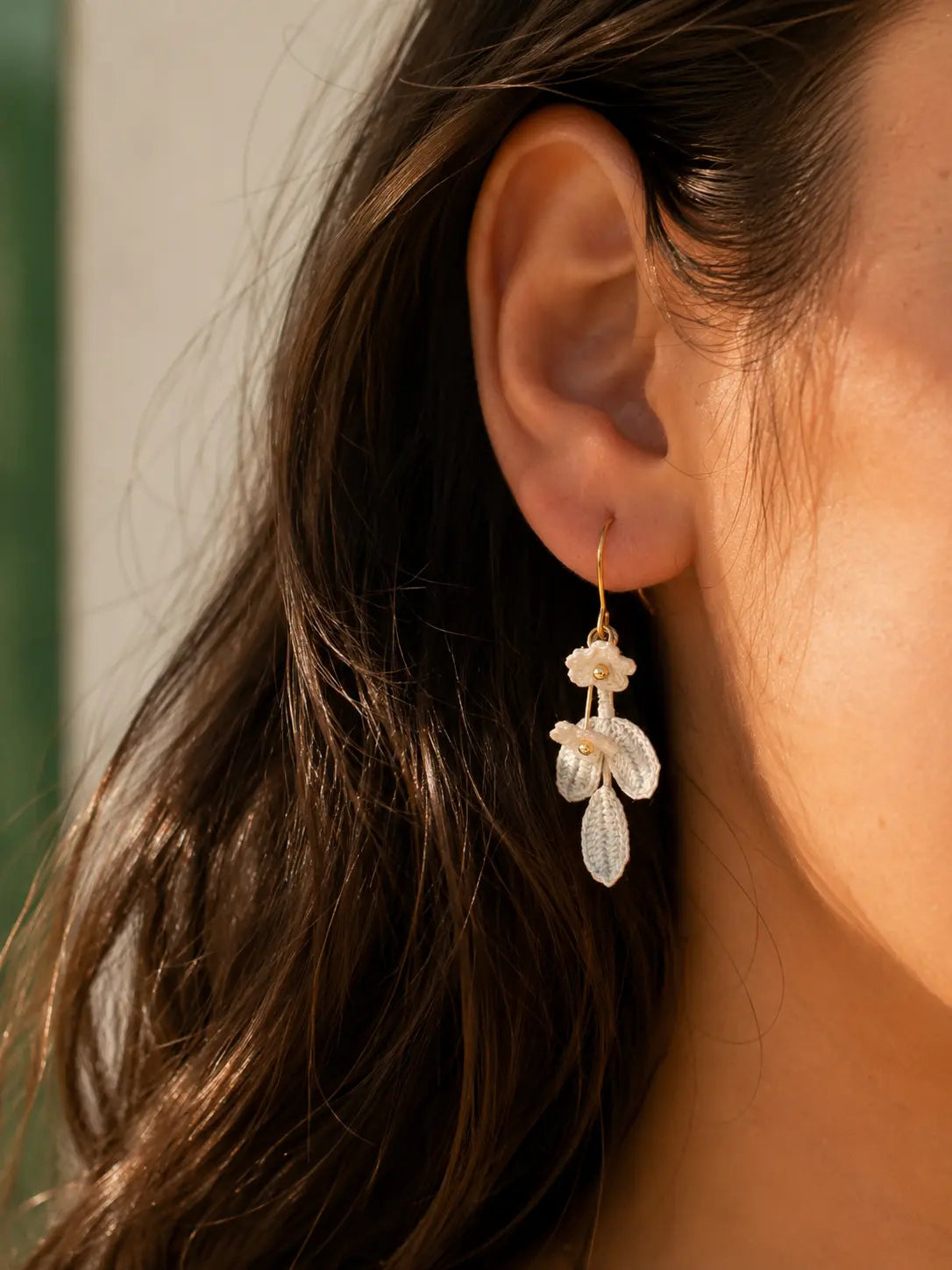 Close-up side view of a brunette woman wearing a white blossom and powder blue crochet leaf drop earring.