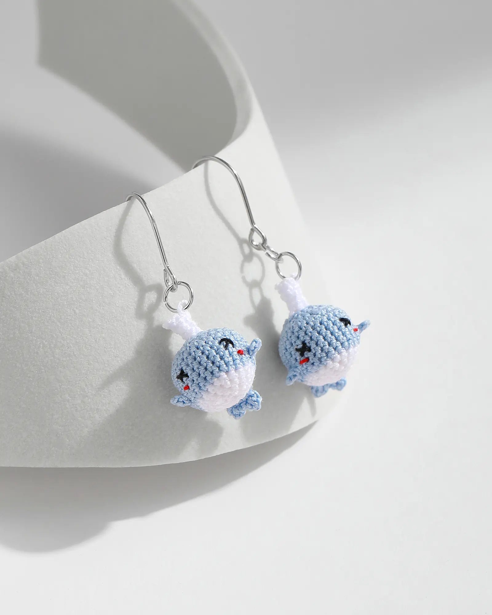 Blue micro crochet whale drop earrings with silver hooks on a white ceramic display