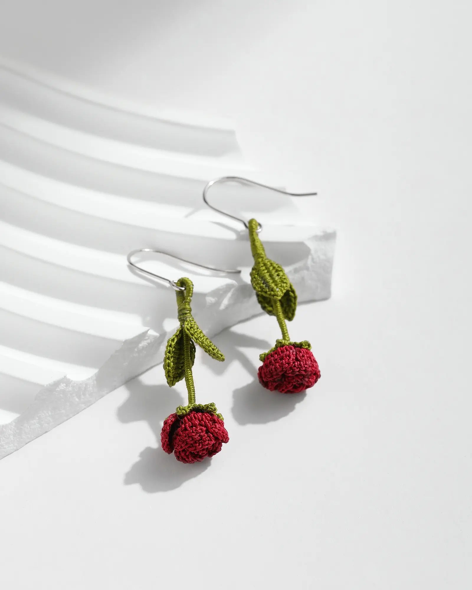 Burgundy Red Rose Bud Drop Earrings with green stems on a white jewellery display