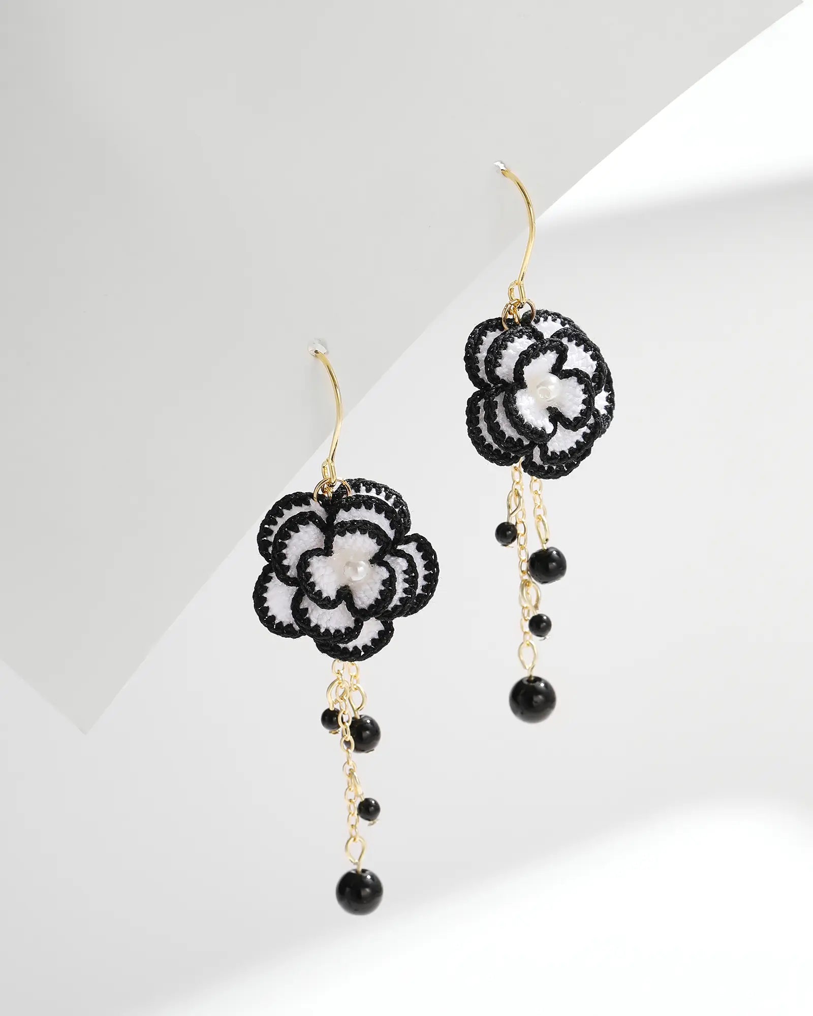 Black-trimmed white micro crochet camellia drop earrings with gold chains and black bead accents on a white background
