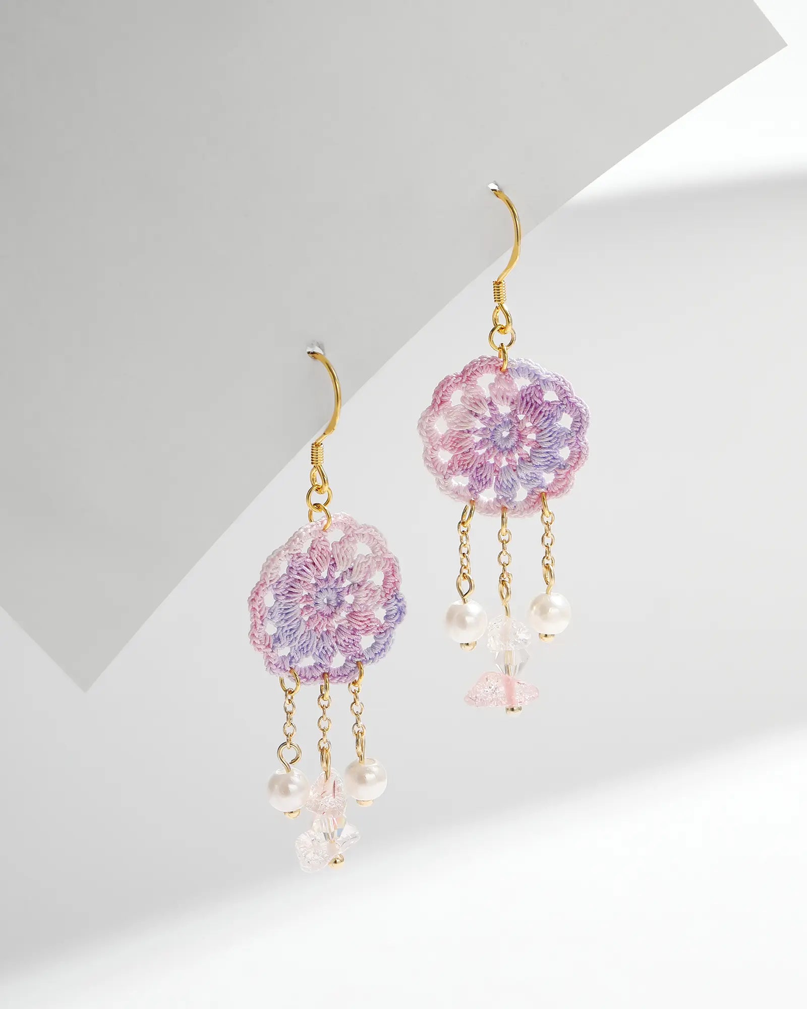 Pair of purple micro crochet dreamcatcher drop earrings with crystal and pearl dangles, gold-tone chains and hooks on a white background.