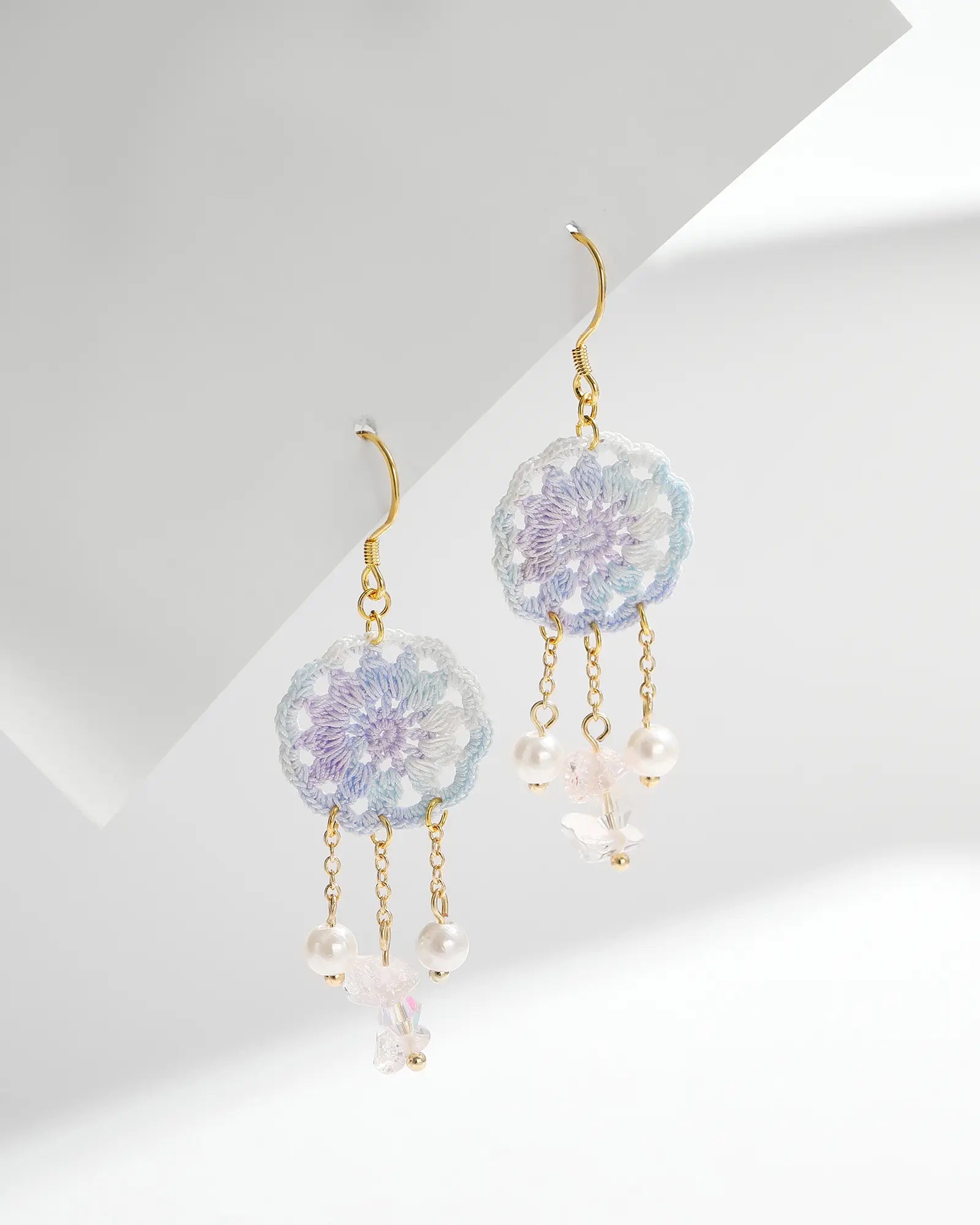 Pair of pale blue micro crochet dreamcatcher drop earrings with crystal and pearl dangles, gold-tone chains and hooks on a white background.
