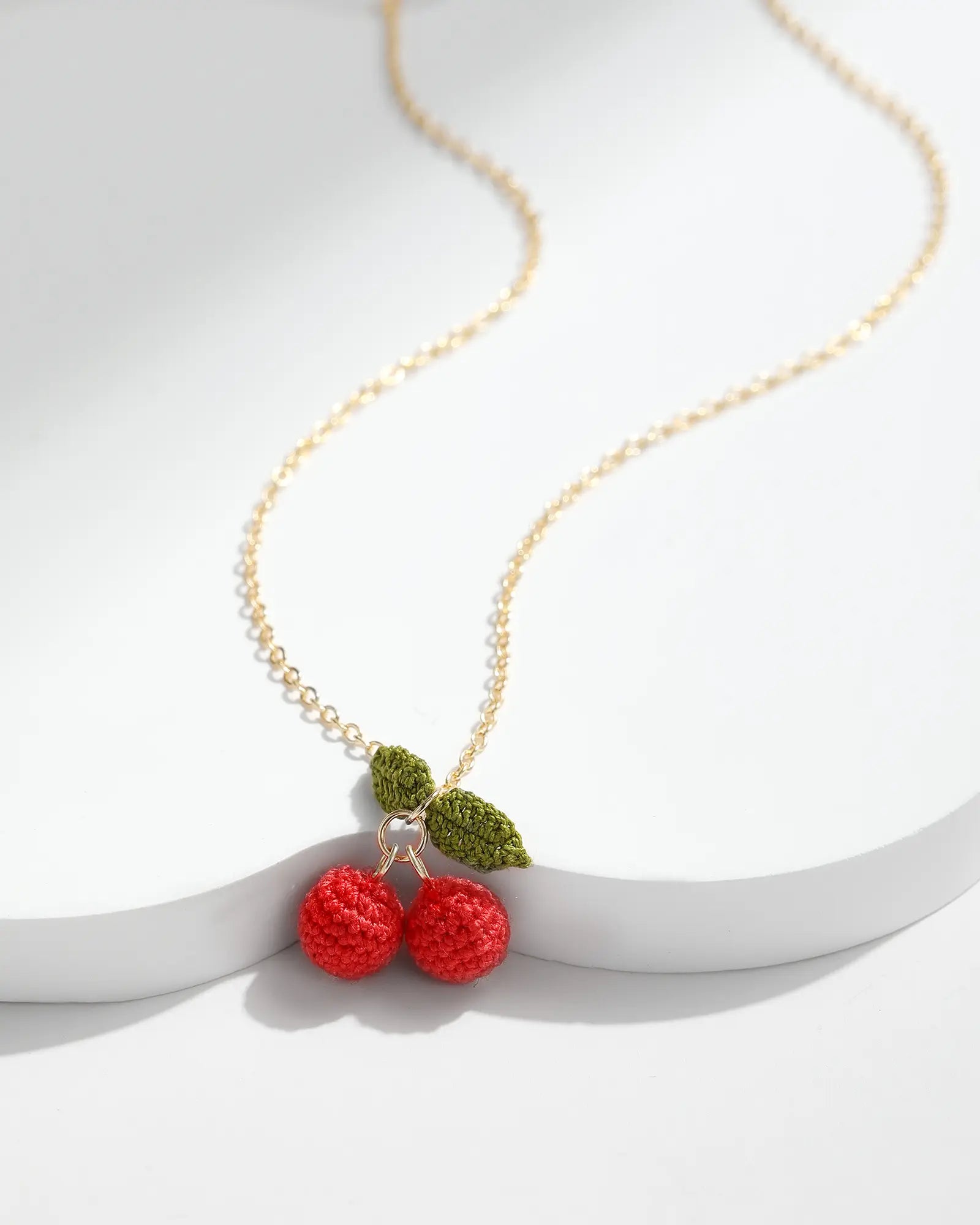 Cherry Necklace featuring two handmade red micro crochet cherries with green leaves on a delicate gold chain.