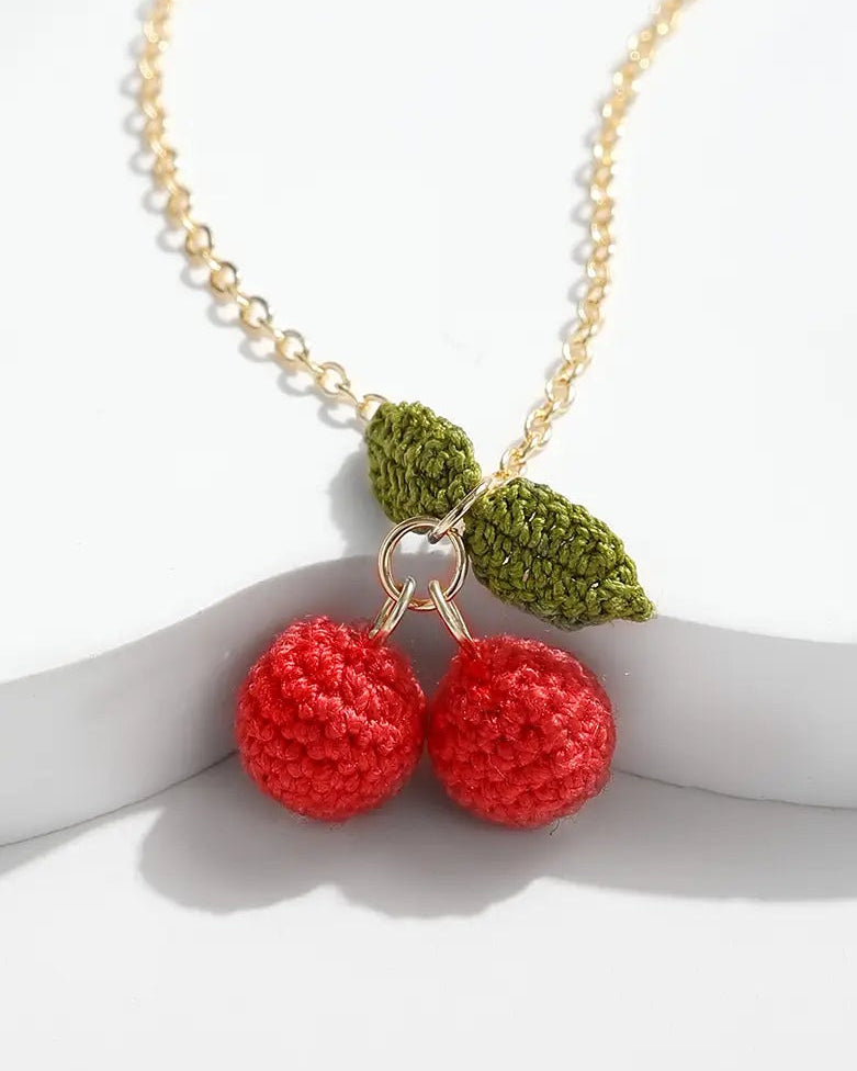 Close-up of a Cherry Necklace with two red micro crochet cherries and green crochet leaves on a gold chain.