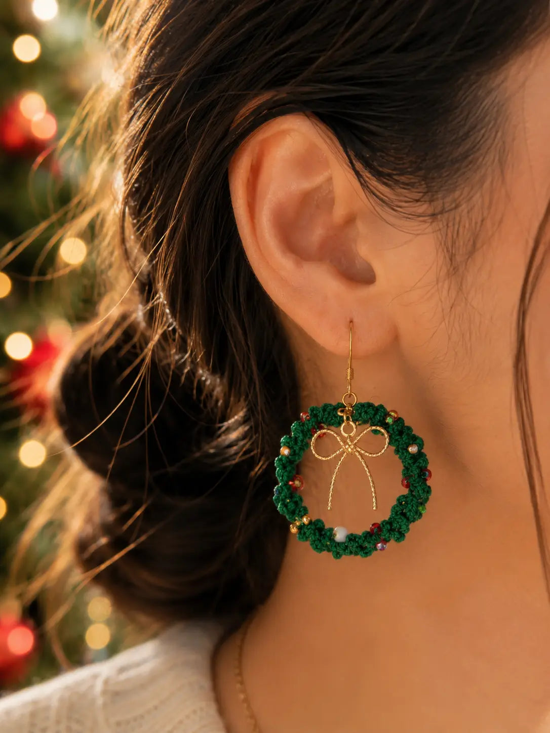 Close-up of a model wearing handmade green Christmas wreath drop earrings with gold bow details