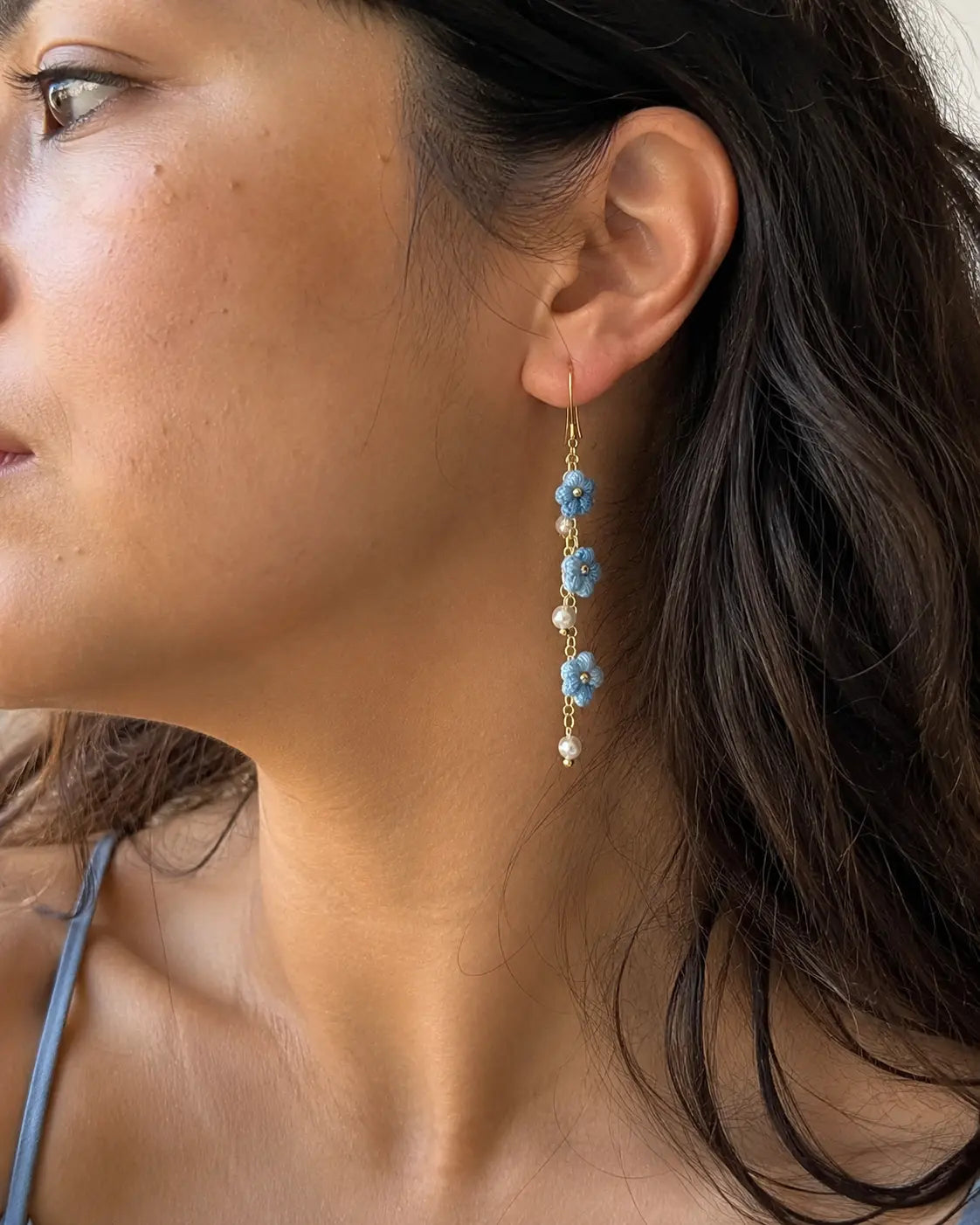 Close-up of woman wearing blue Puff Flower Drop Earrings with gold chain details