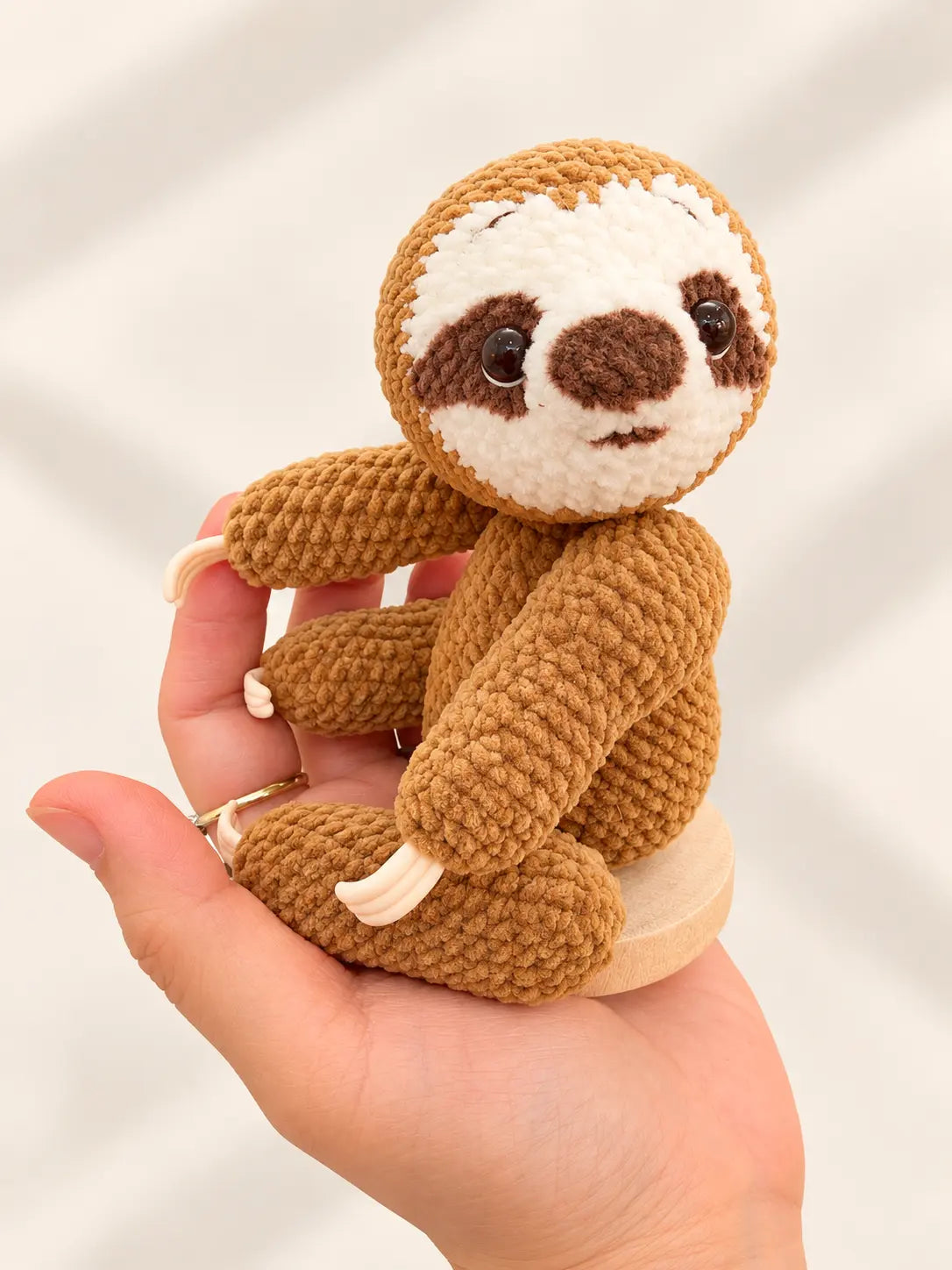 Handmade crochet sloth ornament held in hand, showing its full body, soft texture and original magnetic head and body design.