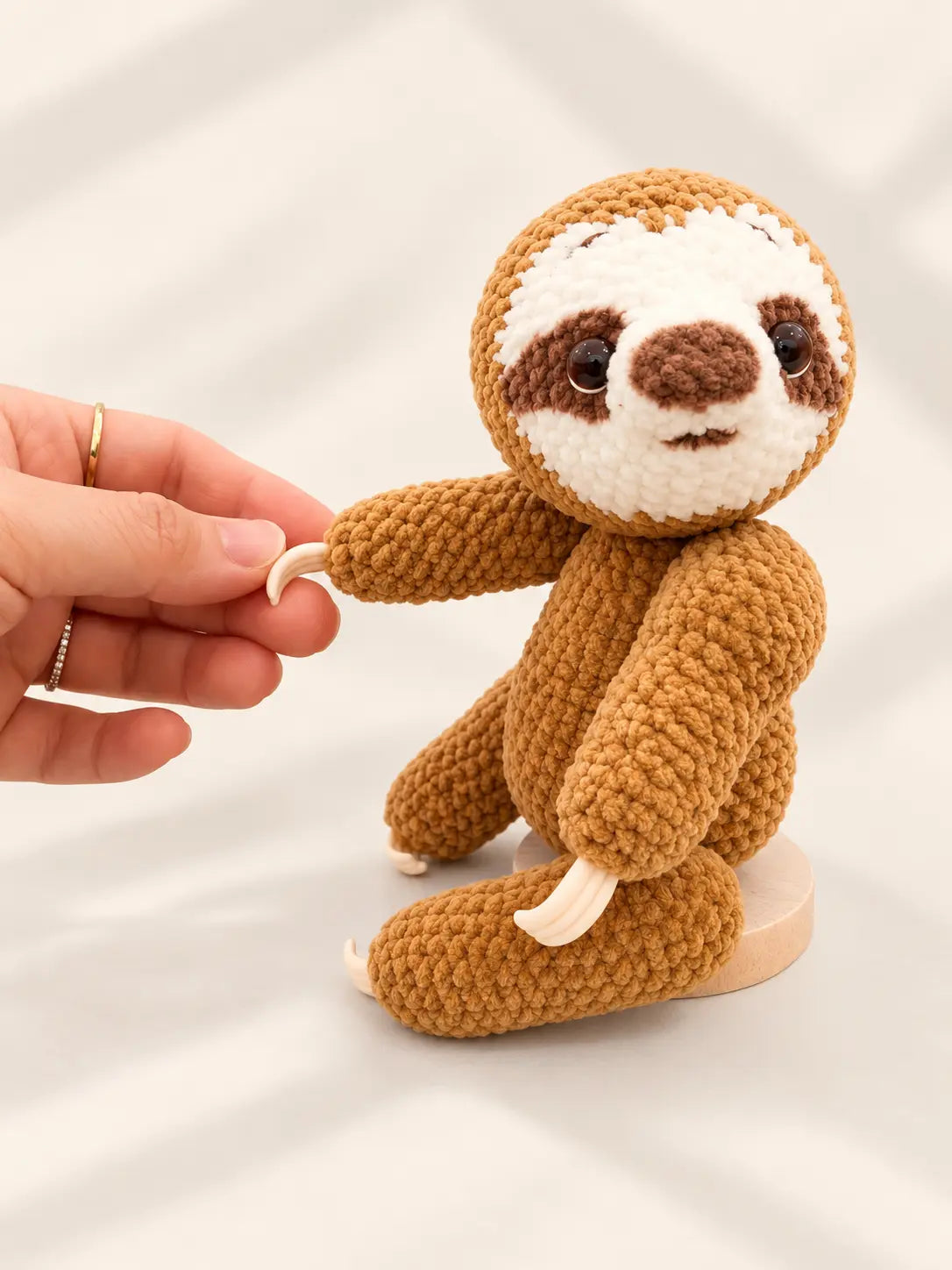 Handmade crochet sloth ornament in a sitting pose, featuring a soft brown body, white face and original magnetic head design.