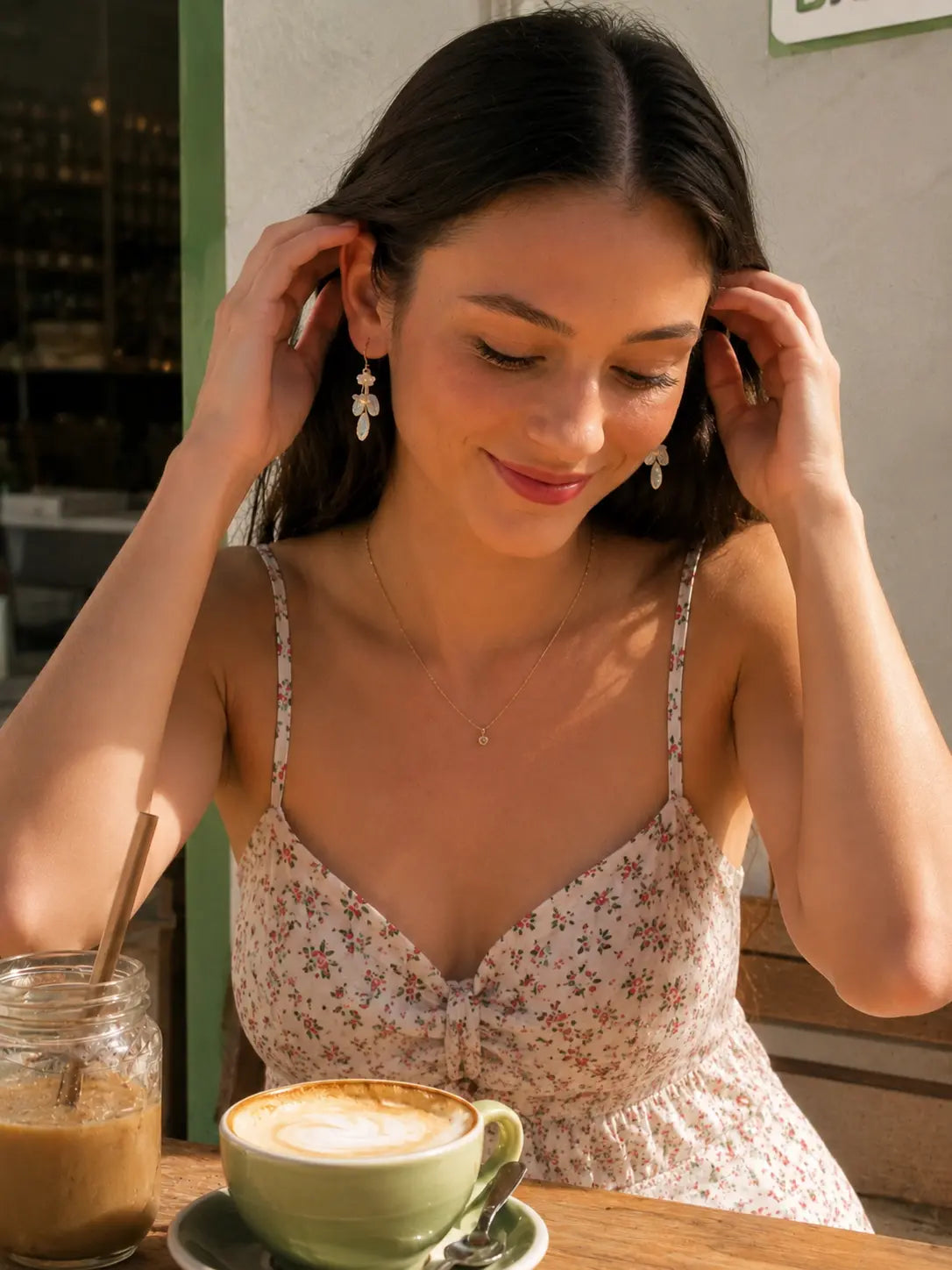 Woman adjusting her hair while wearing powder blue leaf and white blossom crochet earrings at an outdoor café.