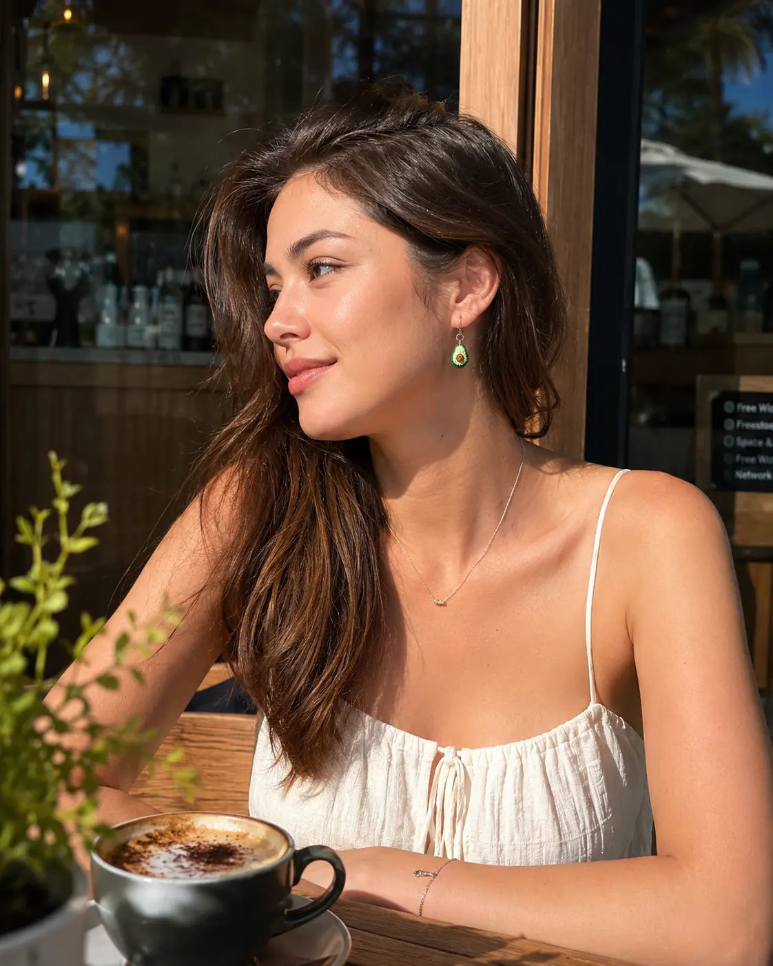 Model wearing micro crochet Avocado Drop Earrings at a sunny café, showing the playful avocado earrings from the side.