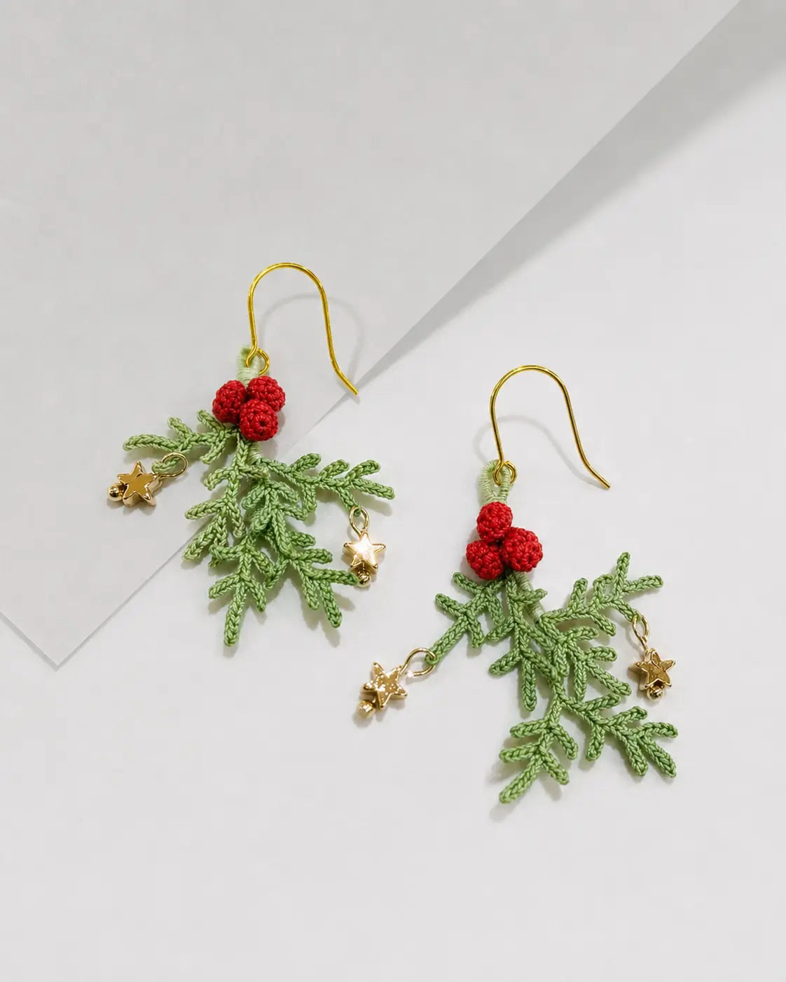 Detailed view of handmade Christmas holly berry and star earrings with red berry clusters, green crochet leaves and gold star accents