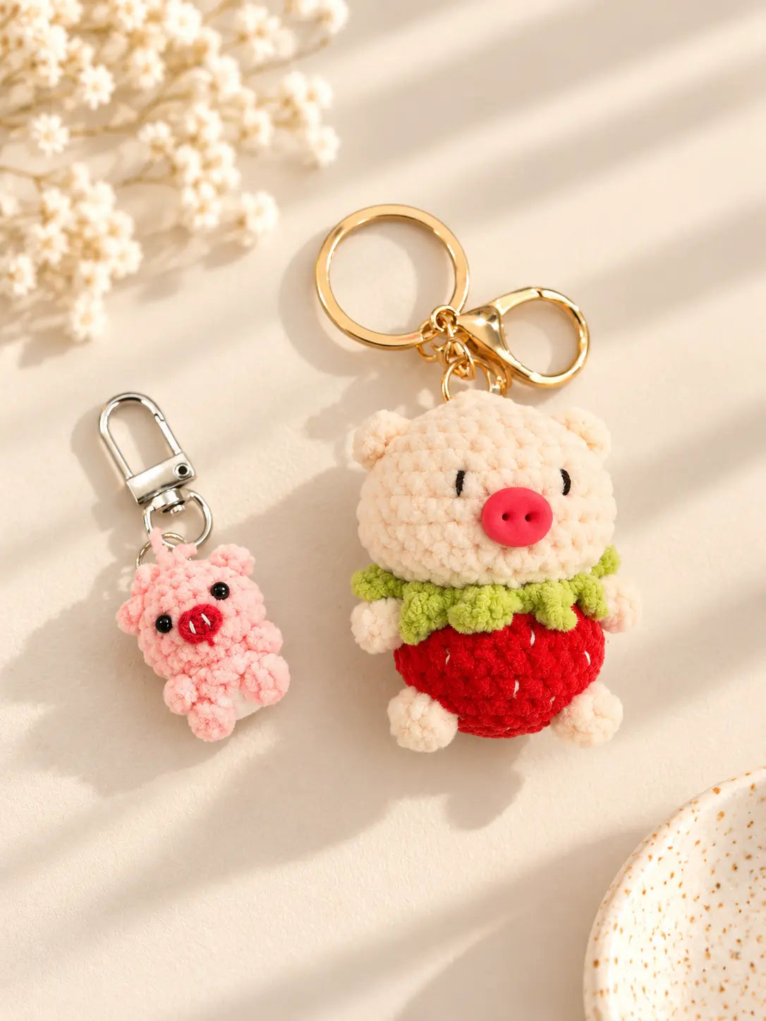 Two cute handmade crochet pig keychains featuring a mini pink pig and a larger pink pig dressed as a strawberry, displayed on a soft cream background.