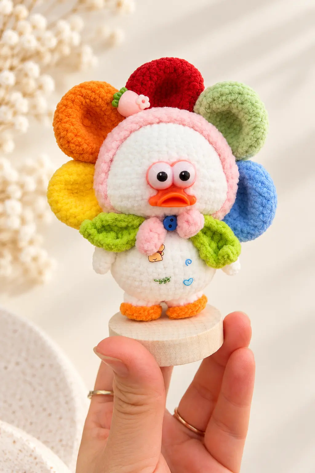 Hand holding a cute handmade crochet flower duck ornament with colourful rainbow petals, a pink duck face and a white body on a small decorative base.