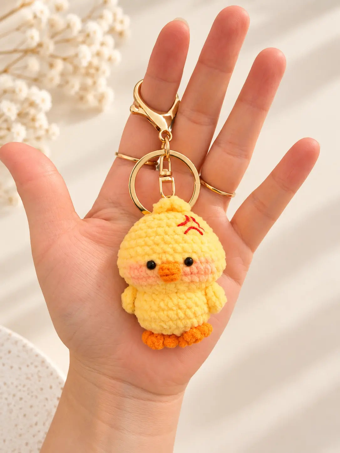 Hand holding a cute handmade yellow crochet grumpy duck keychain with an angry embroidered expression, orange beak and matching feet.