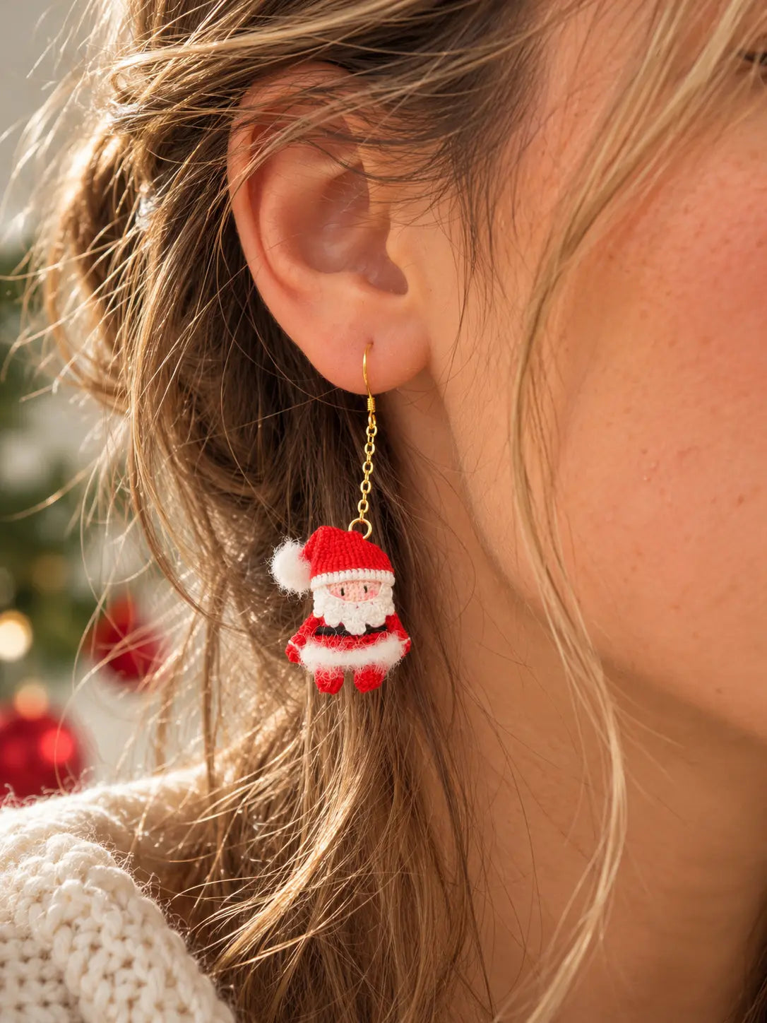 Close-up of a woman wearing a miniature handmade crochet Santa Claus earring, showing its delicate design and how it hangs from the ear.