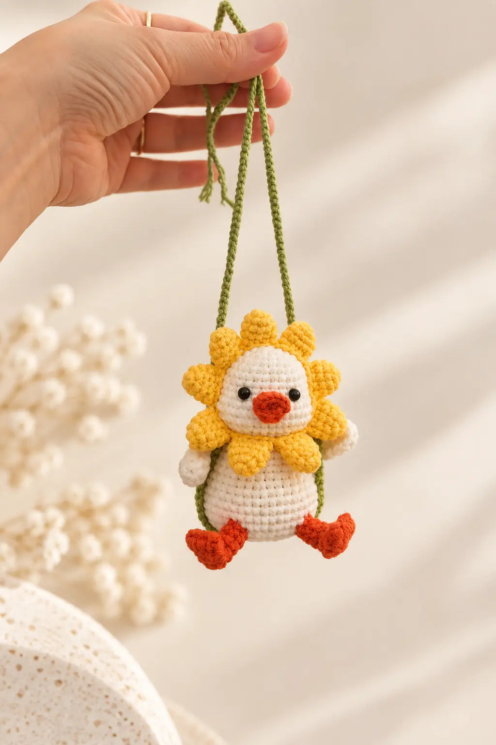Hand holding a handmade crochet swinging duck featuring a little white duck with yellow flower petals, orange feet and a miniature hanging swing.